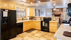 A kitchen with wooden cabinets, a black refrigerator, a stove, and a brick fireplace.