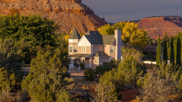 A two-story house with a wrap-around porch, surrounded by trees and a mountainous backdrop.