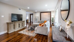 A spacious living room with a flat-screen TV, a grey sofa, and a wooden coffee table. - Preston Hollow Haven (Dallas)