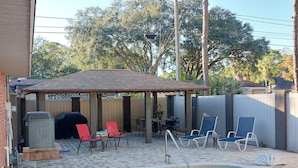 Un jardin avec une piscine, du mobilier de jardin et un espace barbecue.