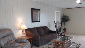 Un salon comprenant un canapé, un fauteuil inclinable, une table basse, une lampe, un tableau encadré et un ventilateur de plafond.