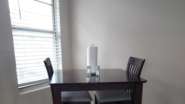Une table à manger avec deux chaises, une bougie et une fenêtre avec des stores.