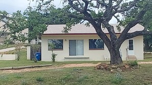 Une maison de plain-pied avec un toit rouge, un porche à l’avant et un grand arbre devant.