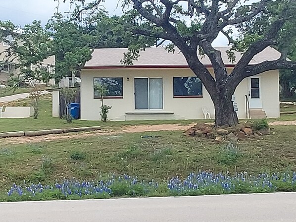 Une maison de plain-pied avec un toit rouge, un porche à l’avant et un grand arbre devant.