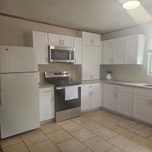 Una cocina con gabinetes blancos, un refrigerador de acero inoxidable, un microondas, un horno y un lavaplatos.