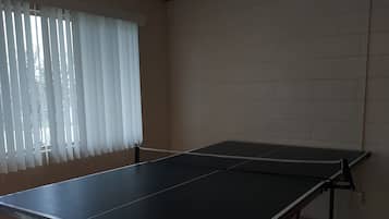 Una stanza con un tavolo da ping pong, una ventola a soffitto e una finestra con tende.