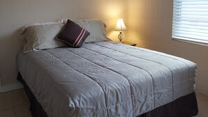 Une chambre à coucher avec un lit, une table de chevet, une lampe et une fenêtre avec des stores.