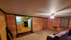 A room with a wooden interior, a ceiling fan, a sofa, and a view into a kitchen area. - Secluded camp off the snowmobile trail (New Sweden)