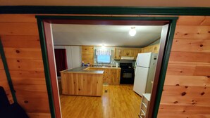 A wooden interior with a kitchen area featuring wooden cabinets, a refrigerator, and a stove. - Secluded camp off the snowmobile trail (New Sweden)