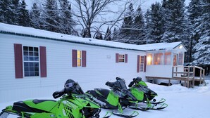 A row of snowmobiles parked in front of a white building with red shutters. - Secluded camp off the snowmobile trail (New Sweden)