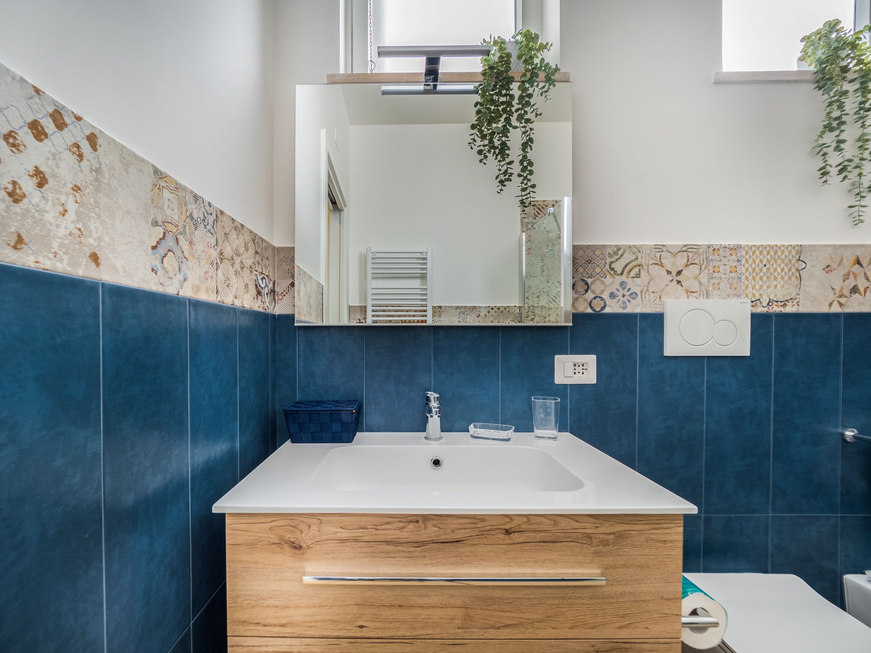A bathroom with a white sink, wooden vanity, and blue tiles.