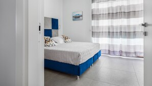A bedroom with a bed, a headboard with a geometric pattern, a wall-mounted picture, and a window with a striped curtain. - Azzurro Park Suite Sorrento (Sorrento)