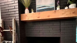 A fireplace with a wooden mantel shelf, a framed picture, and a potted plant. - Mid-Century Modern Montana Dream Home (Butte)