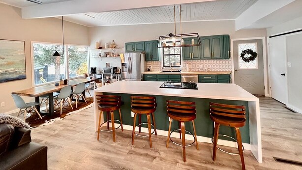 A spacious kitchen with a large island, green cabinets, and a modern pendant light. - Mid-Century Modern Montana Dream Home (Butte)