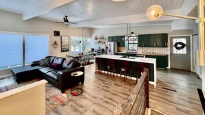 A spacious living area with a black leather sofa, a dining area with bar stools, and a kitchen with green cabinets and a white countertop. - Mid-Century Modern Montana Dream Home (Butte)
