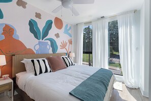 A bedroom with a bed, a ceiling fan, a nightstand, a lamp, and a view of the outdoors through a window. - The Grove by AvantStay – Stylish Group Stay with Private Bathrooms (Nashville)