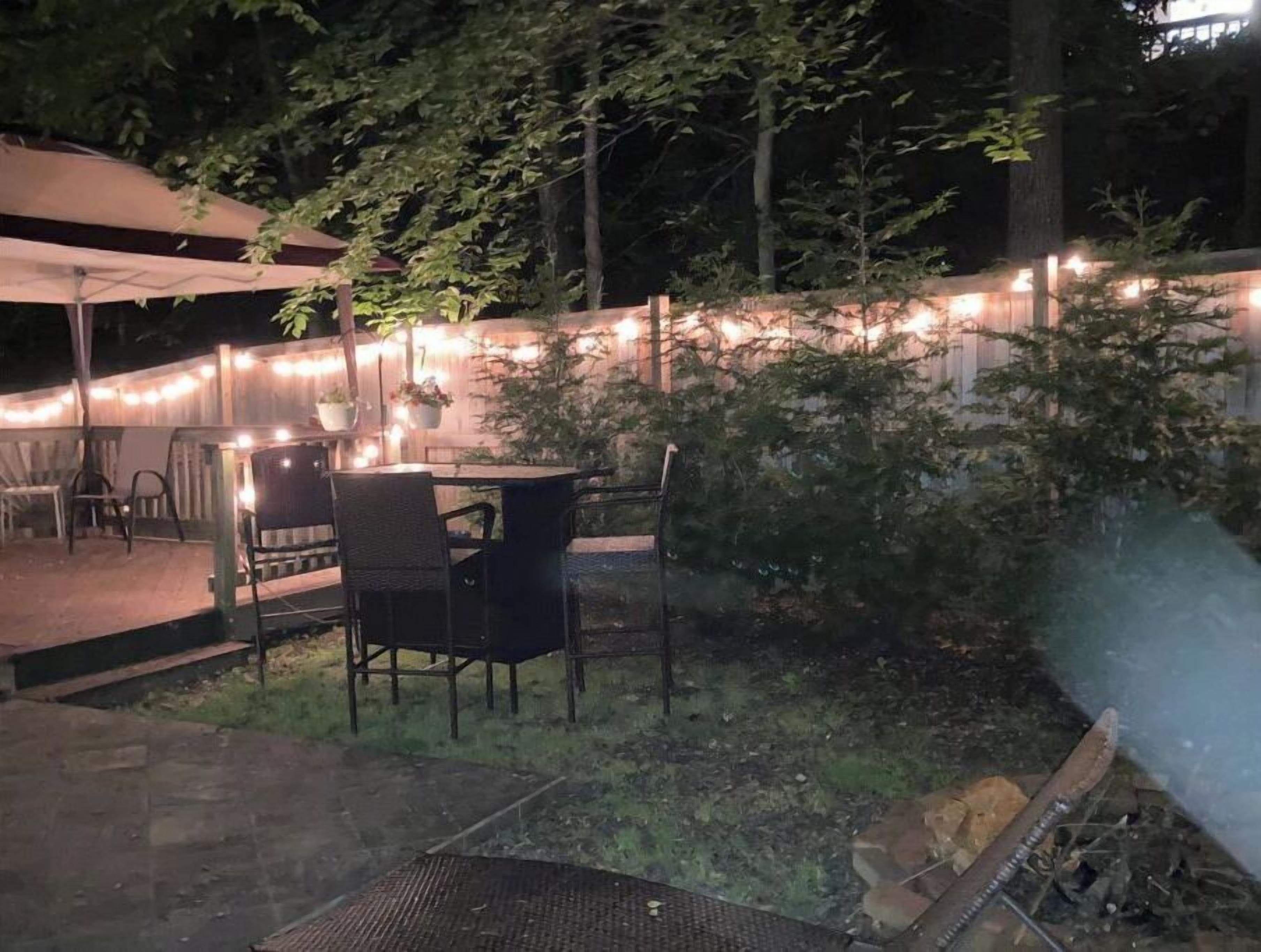 An outdoor patio area with a table and chairs, surrounded by a wooden fence and string lights.