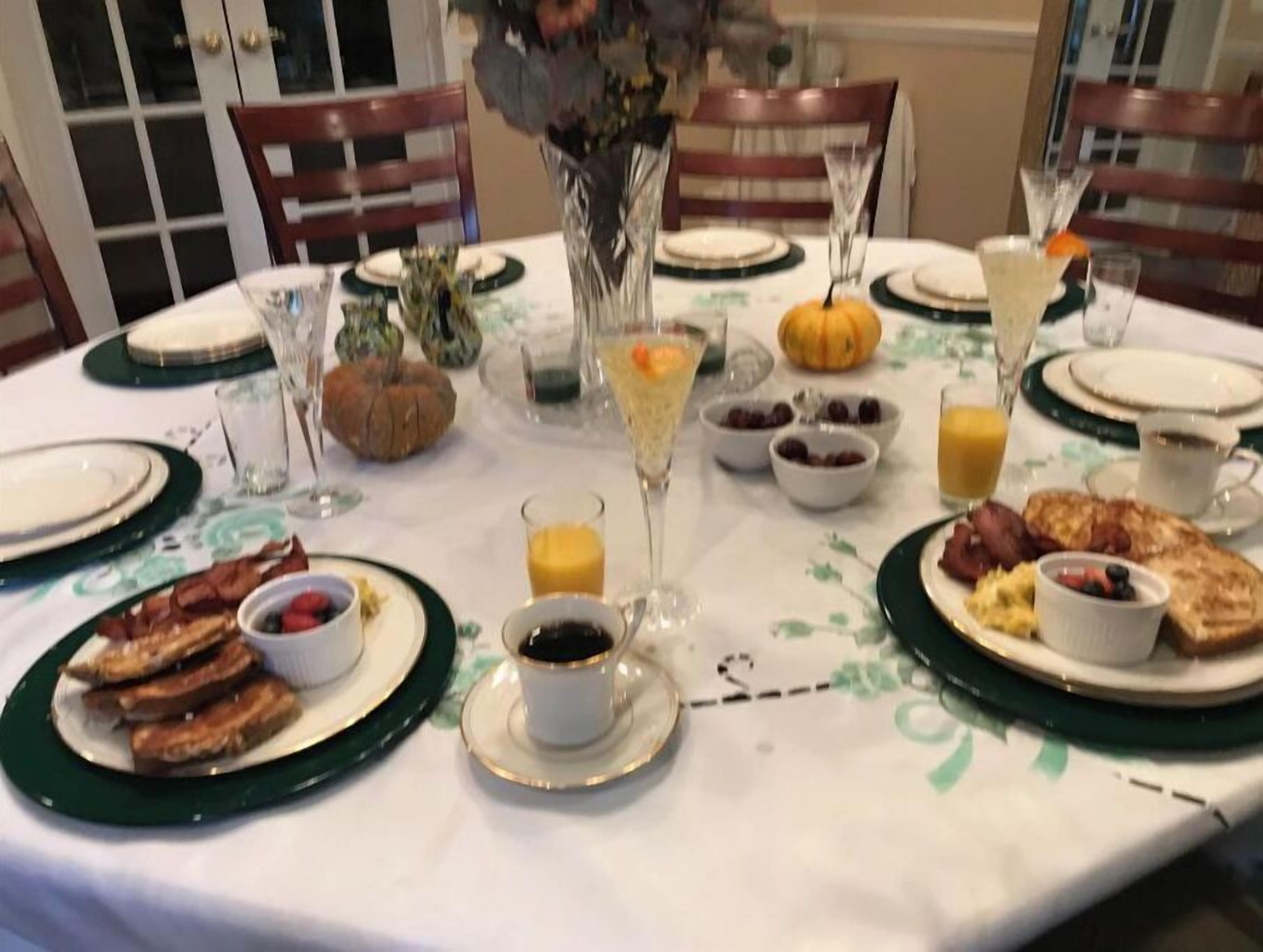 A breakfast setting with plates of bacon, eggs, and toast, along with various fruits and beverages.