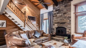 Una sala de estar acogedora con chimenea de piedra, mobiliario de cuero y una escalera de madera.