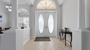 A clean, white hallway with a double door, a bench, and a small table with a plant.