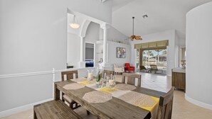 A dining area with a wooden table, beige placemats, candles, and a vase with flowers.