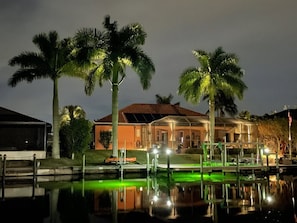 A house with a pool and palm trees at night.