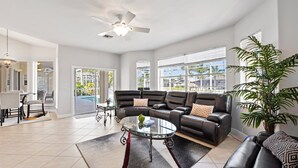 A spacious living room with a large sectional sofa, a glass coffee table, and a ceiling fan.