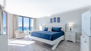 Ein modernes Schlafzimmer mit einem großen Bett, einer Sitzecke mit einem Sessel, einem Nachttisch und einer Kommode.