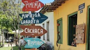 A row of colorful directional signs in front of a yellow building with green shutters. - Sea View House, Luxury and Comfort (Porto Seguro)