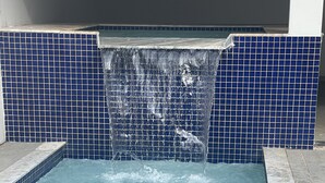 A swimming pool with a waterfall feature, surrounded by blue-tiled walls. - Sea View House, Luxury and Comfort (Porto Seguro)