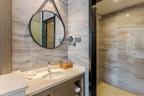 A modern bathroom with a marble vanity, a round mirror, and a glass-enclosed shower.
