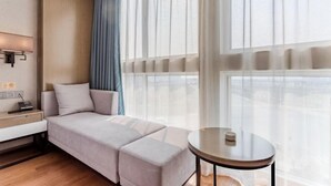 Una habitación de hotel moderna con un sofá cama, una mesita de noche con lámpara y una mesa redonda.