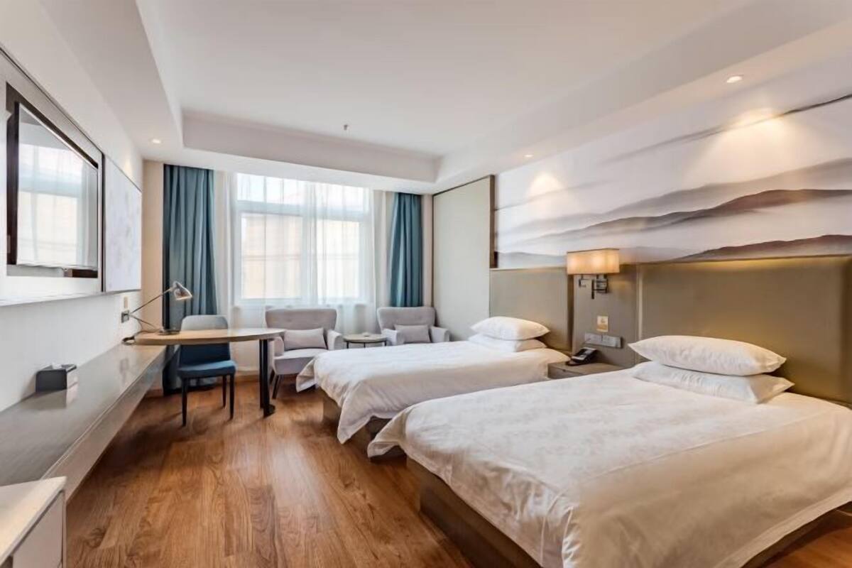 A hotel room with two beds, a desk, a chair, and a large window with curtains.