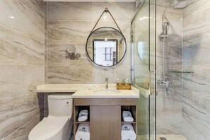 A modern bathroom with a marble wall, a round mirror, a toilet, a sink with a vanity, and a glass-enclosed shower.