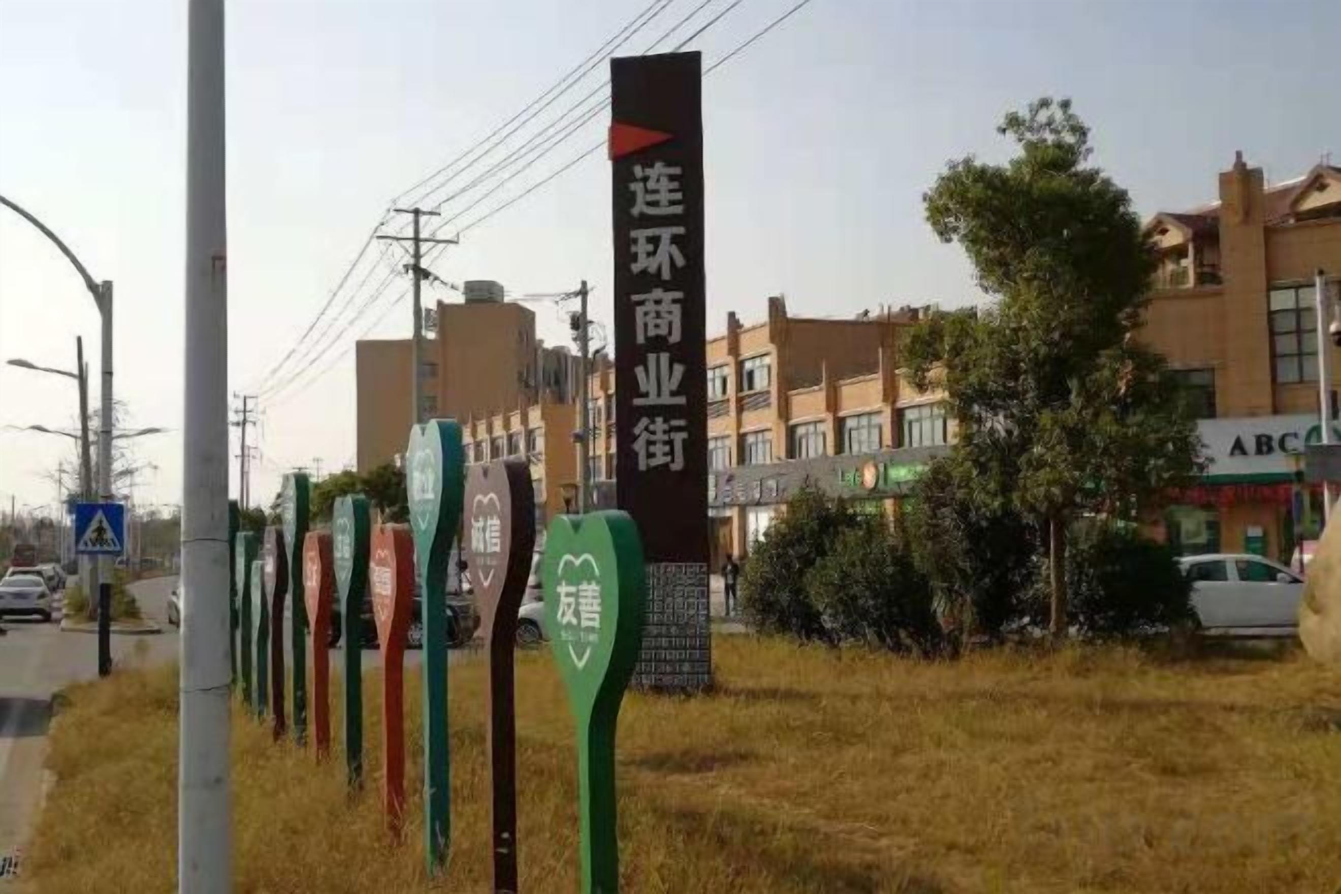 Eine Reihe von Hinweisschildern mit chinesischen Schriftzeichen, ein Gebäude mit einer Schautafel sowie eine Straße mit Gebäuden im Hintergrund.