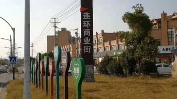 Eine Reihe von Hinweisschildern mit chinesischen Schriftzeichen, ein Gebäude mit einer Schautafel sowie eine Straße mit Gebäuden im Hintergrund.