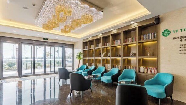 Un lobby moderno con candelabro, estanterías, sillas color turquesa y suelo de mármol.