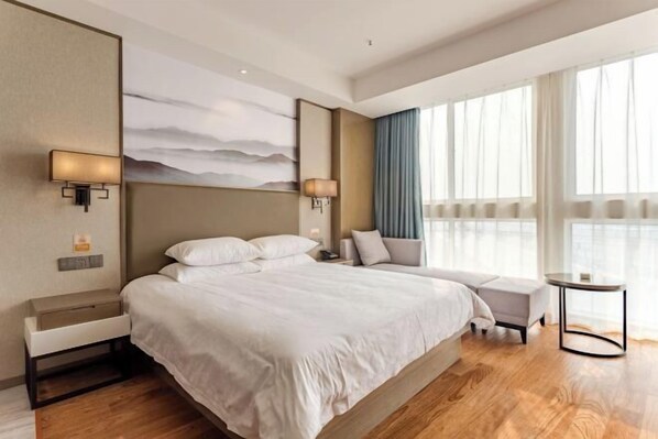 Una habitación de hotel moderna con una cama grande, una mesita de noche, un pequeño sofá y una mesita redonda.