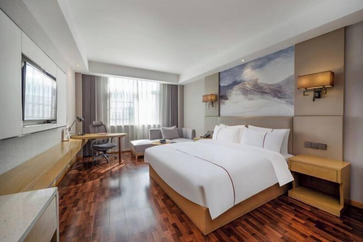 A hotel room with a large bed, a desk, a chair, a TV, and a painting on the wall.