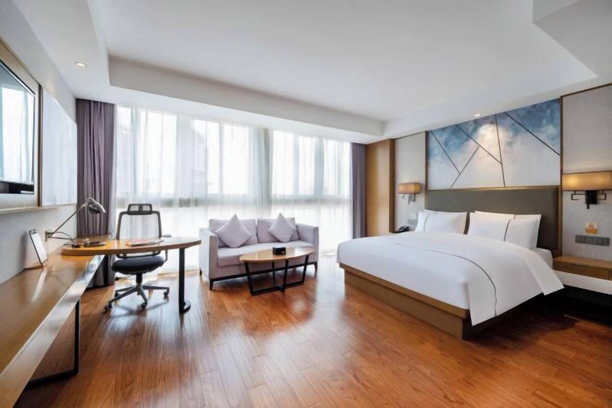 A hotel room with a bed, a desk, a sofa, and a large window.