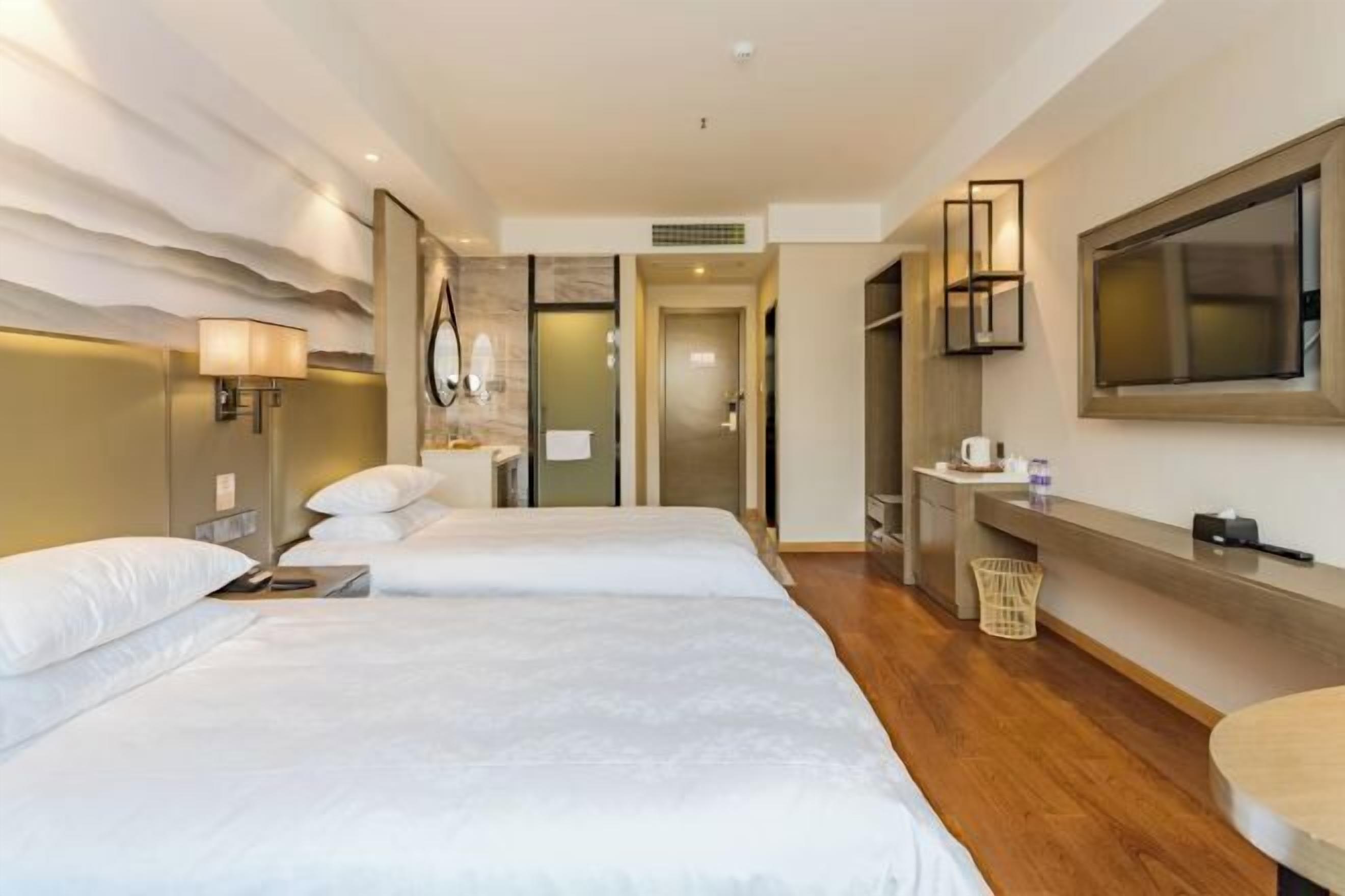 A hotel room with two beds, a large mirror, a TV, and a small desk with a basket.