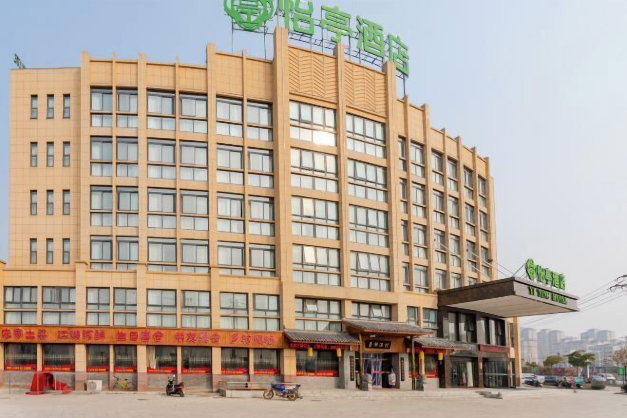 A multi-story hotel with a modern architectural design, featuring a prominent entrance with a covered area and several ground-level shops.
