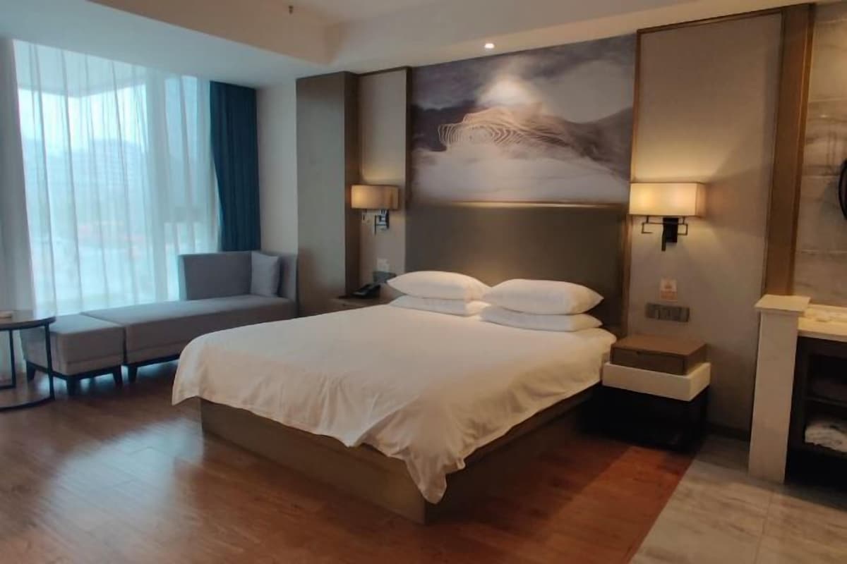 A hotel room with a large bed, a sofa, a desk, and a painting on the wall.