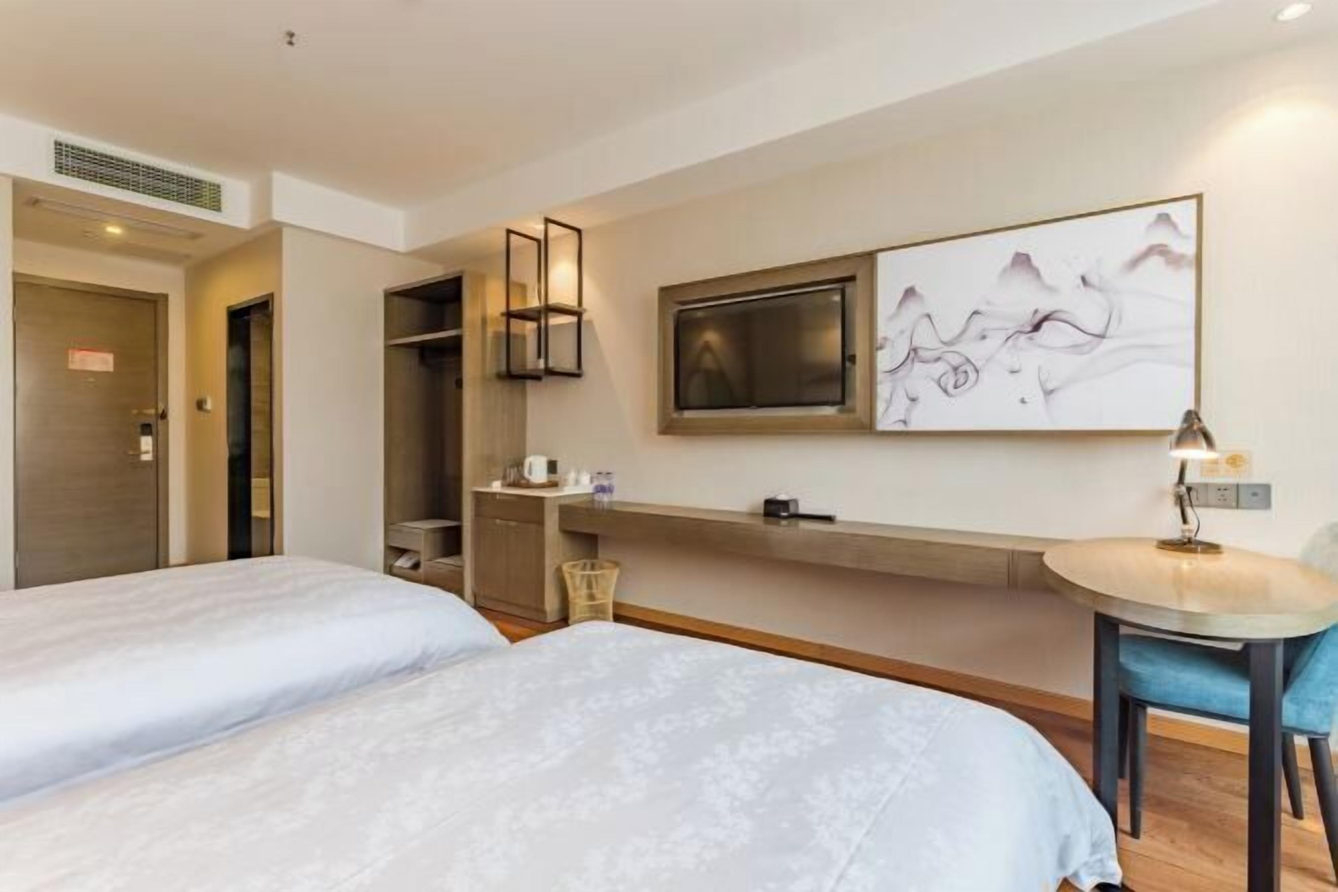 A hotel room with two beds, a desk, a chair, a TV, and a wall-mounted artwork.