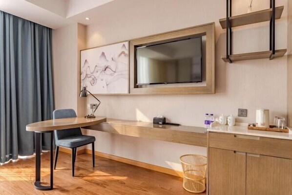 A modern hotel room with a wooden desk, a chair, a flat-screen TV mounted on the wall, a small shelf with toiletries, and a woven basket on the floor. - Yiting Hotel (Hefei Economic Development Zone) (Hefei)
