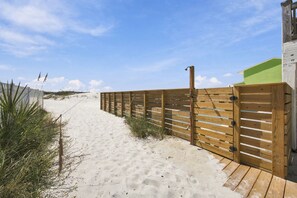 A sandy beach path with a wooden fence and a building with a green roof. - Oceanfront Retreat | 4 King Beds + Private Pool (Gulf Shores)