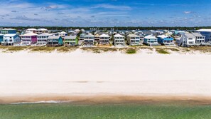 A beachfront property with multiple colorful houses, a sandy beach, and a clear view of the ocean. - Oceanfront Retreat | 4 King Beds + Private Pool (Gulf Shores)
