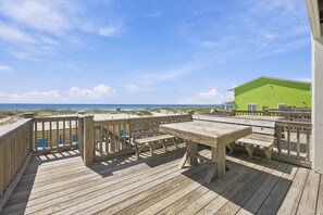A wooden deck with picnic tables and benches, overlooking a beach and a green building. - Luxury Beach House w/ Pool & Stunning Ocean Views (Gulf Shores)
