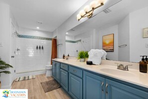 A modern bathroom with a double sink vanity, a shower, and a large mirror.
