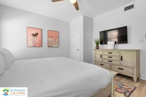 Une chambre à coucher comprenant un lit, une commode, un téléviseur et deux tableaux accrochés au mur.